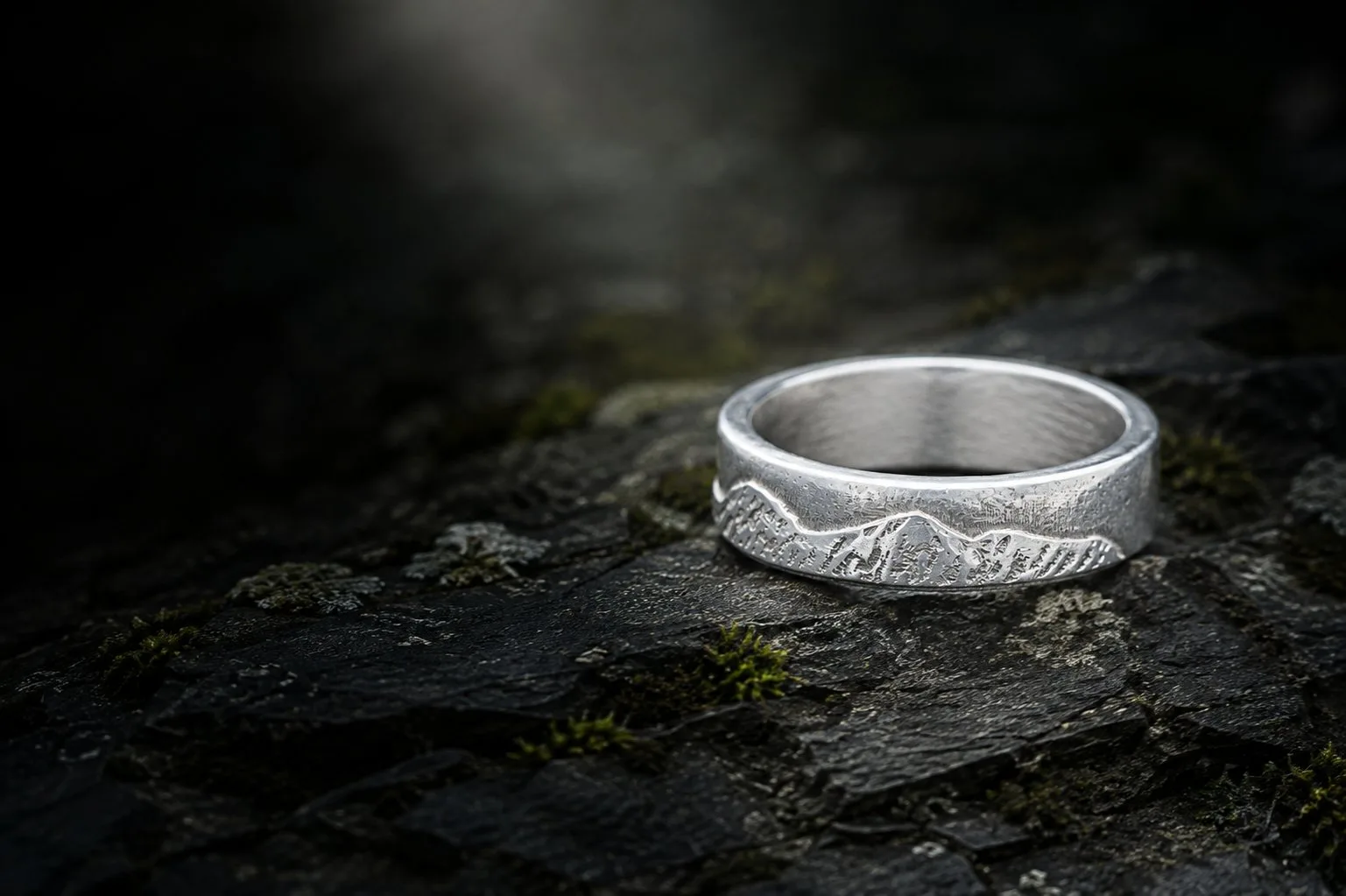 The National Three Peaks silver ring resting on dark weathered slate among moss, in low evening light.