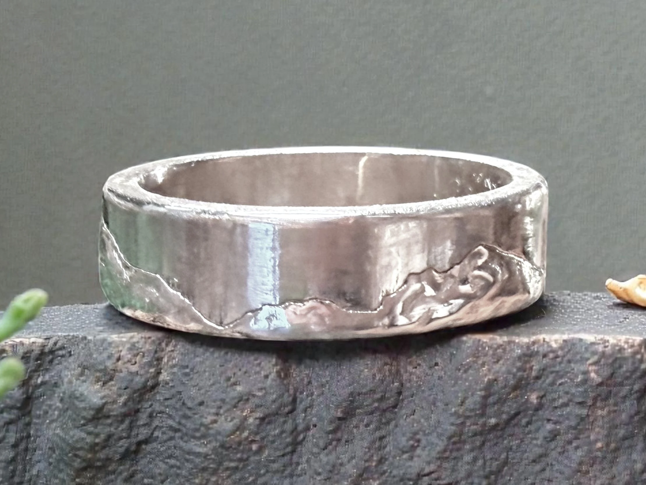 The ring on rough dark stone, the hand-finished slopes running below the bright polished top edge.
