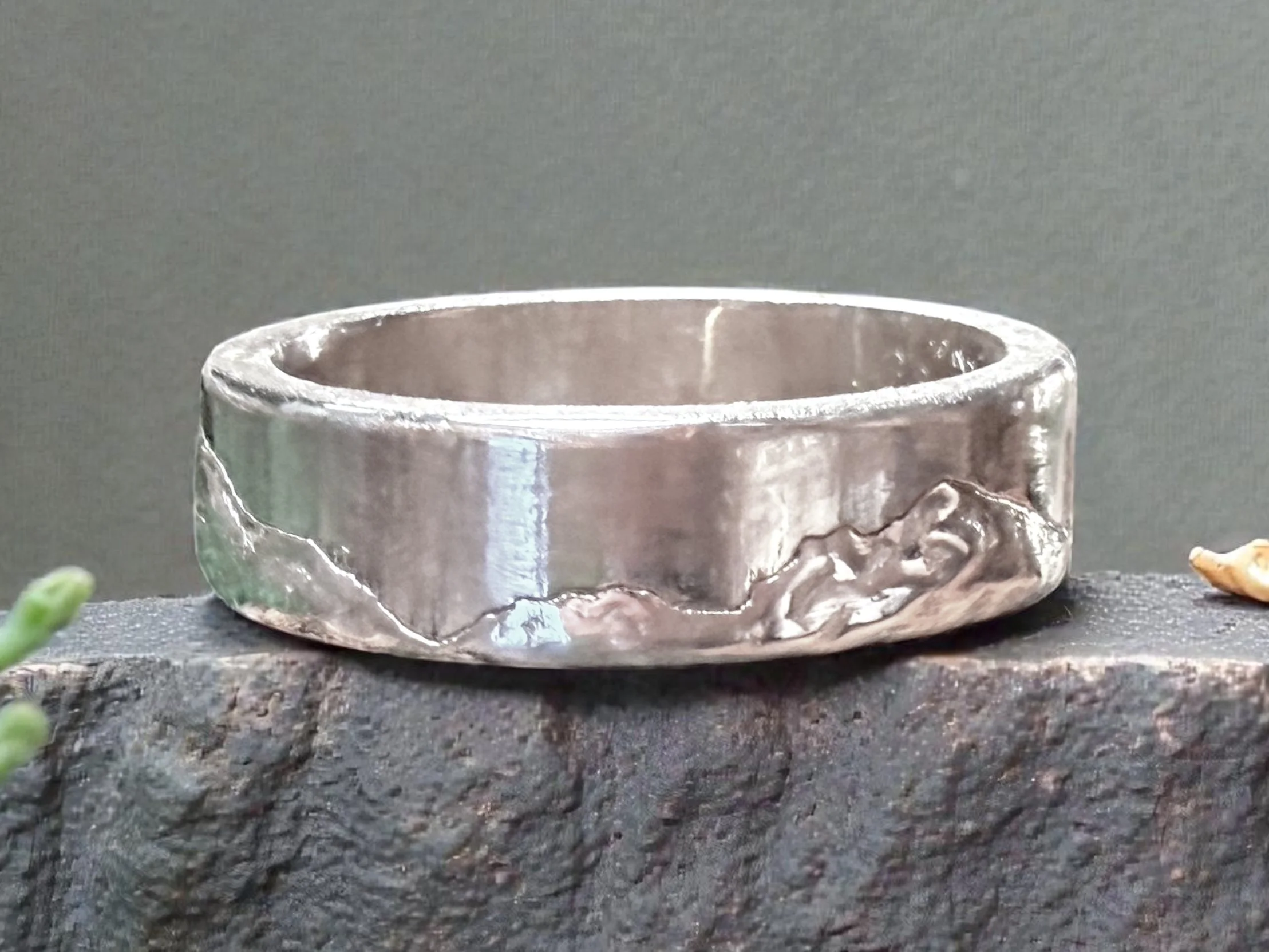 The ring on rough dark stone, the hand-finished slopes running below the bright polished top edge.