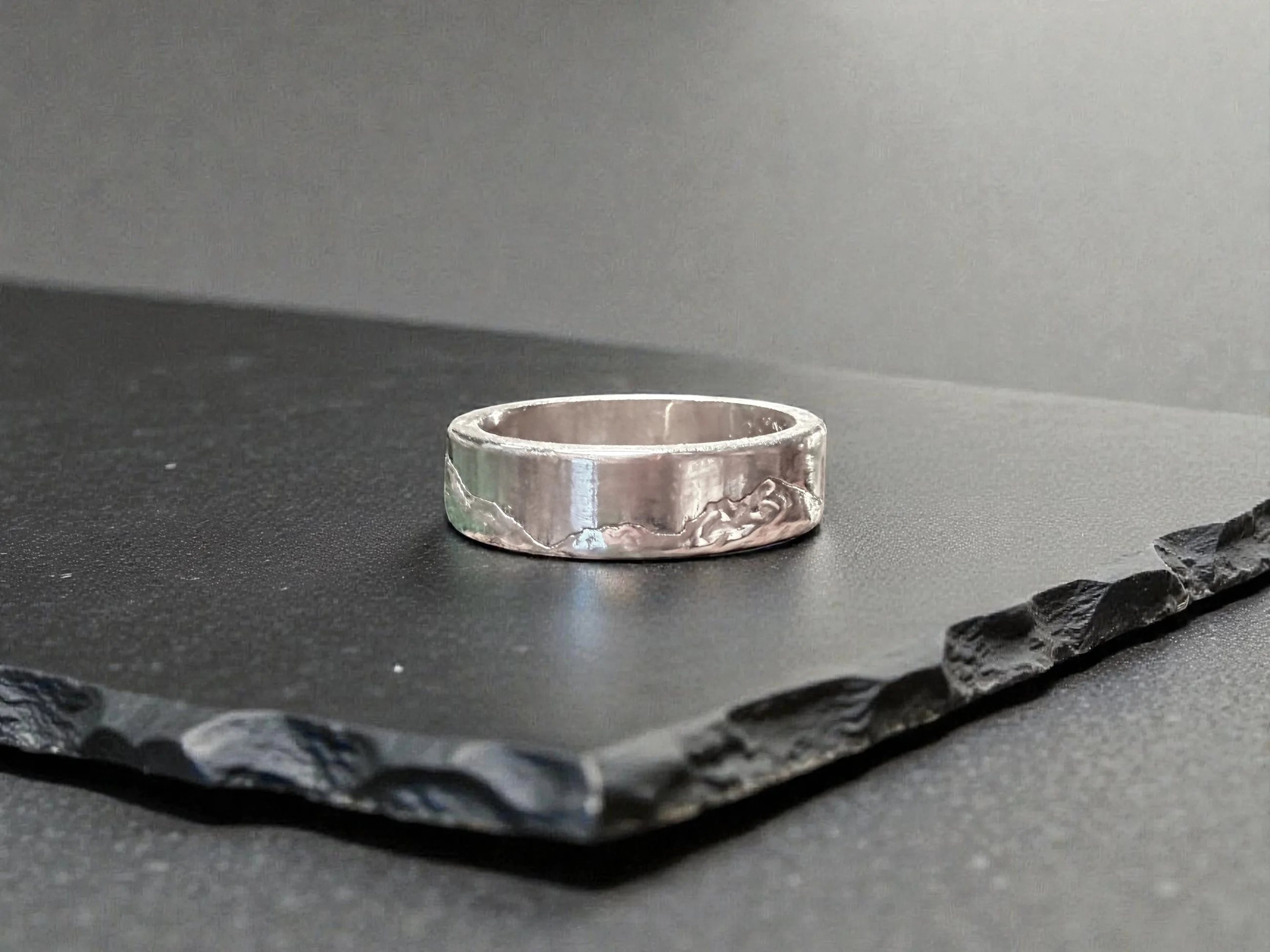 The ring standing on slate, seen from further back, showing the depth and squared edge of the band.