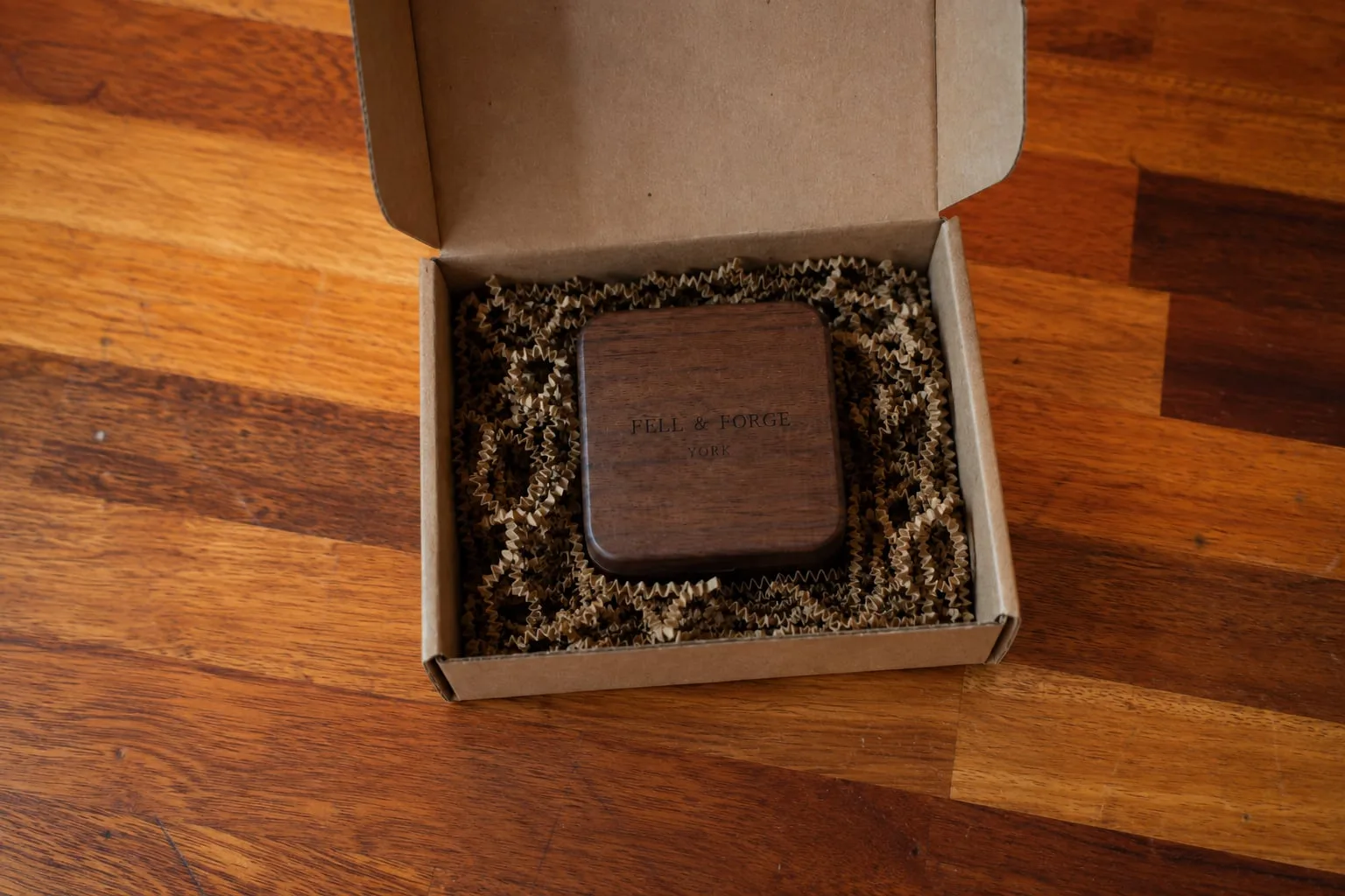 An open kraft shipping box with a walnut ring box marked Fell and Forge, York, nested in protective packing.