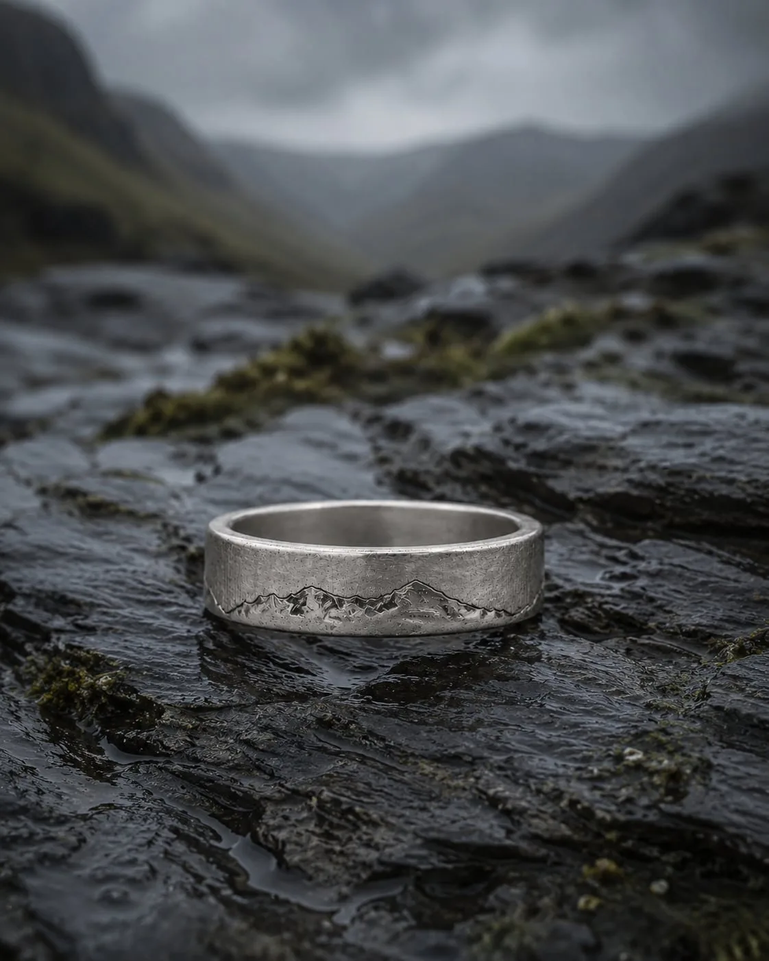 Welsh Three Peaks ring resting on wet dark slate, a misted valley behind it.
