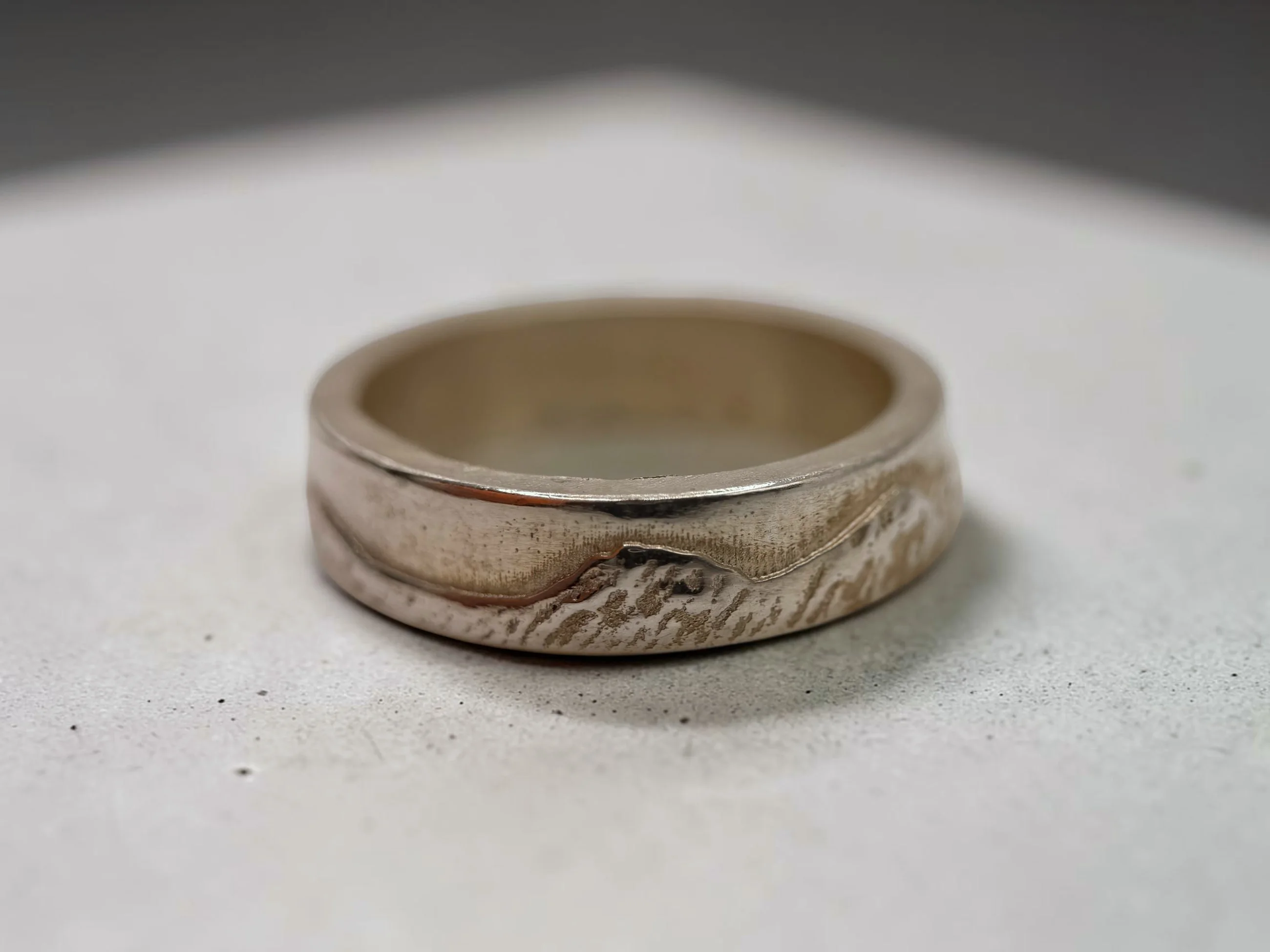 Welsh Three Peaks ring on pale concrete, the raised cast ridge running across the band with a notch at the col.