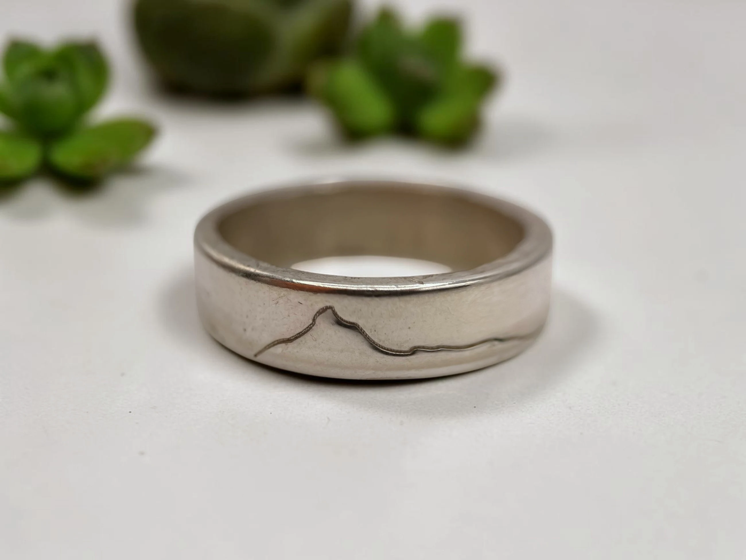The ring photographed among succulents on a pale surface.