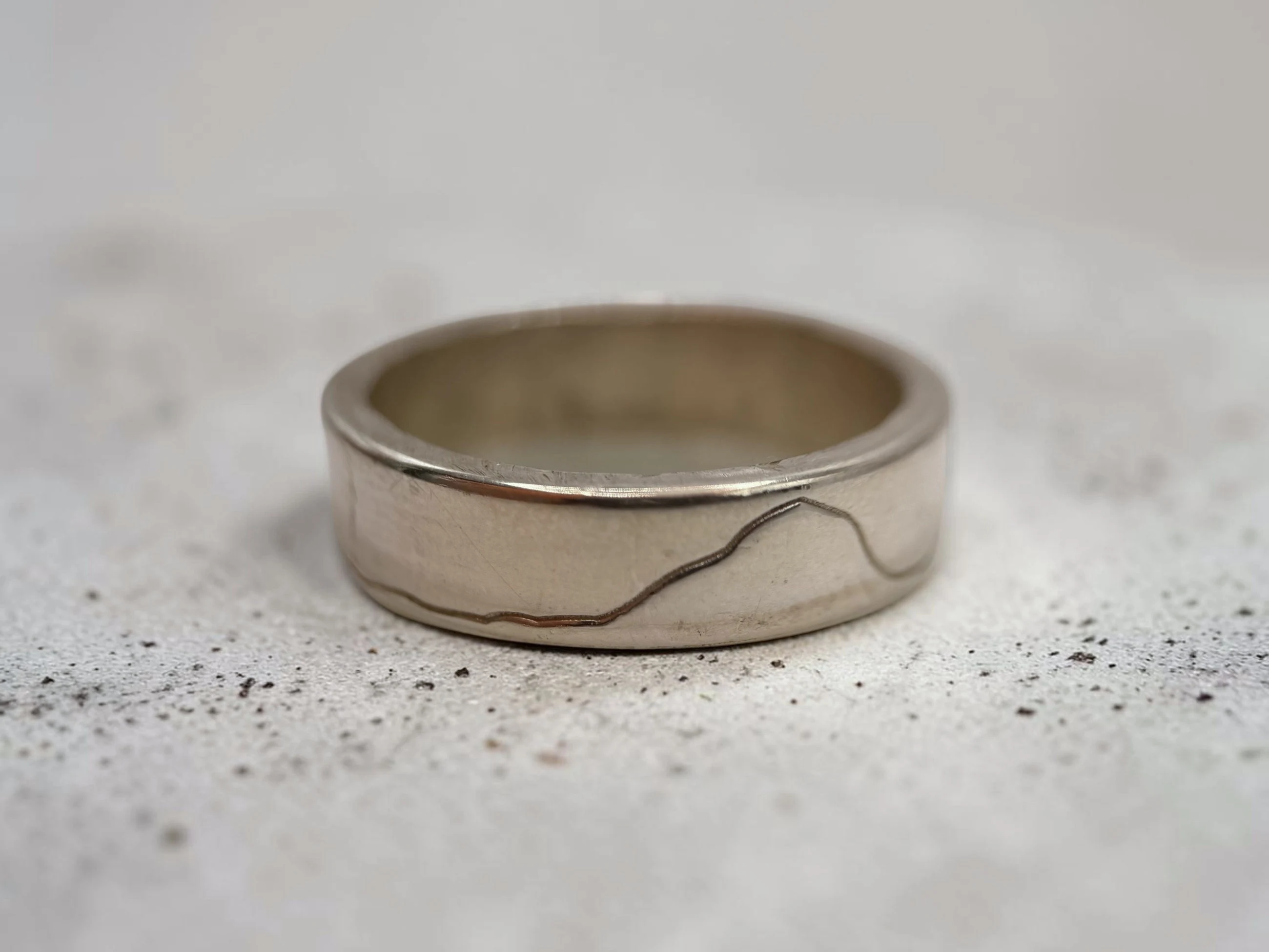 Yorkshire Three Peaks ring on a pale speckled surface, the fine engraved line running low across the band.
