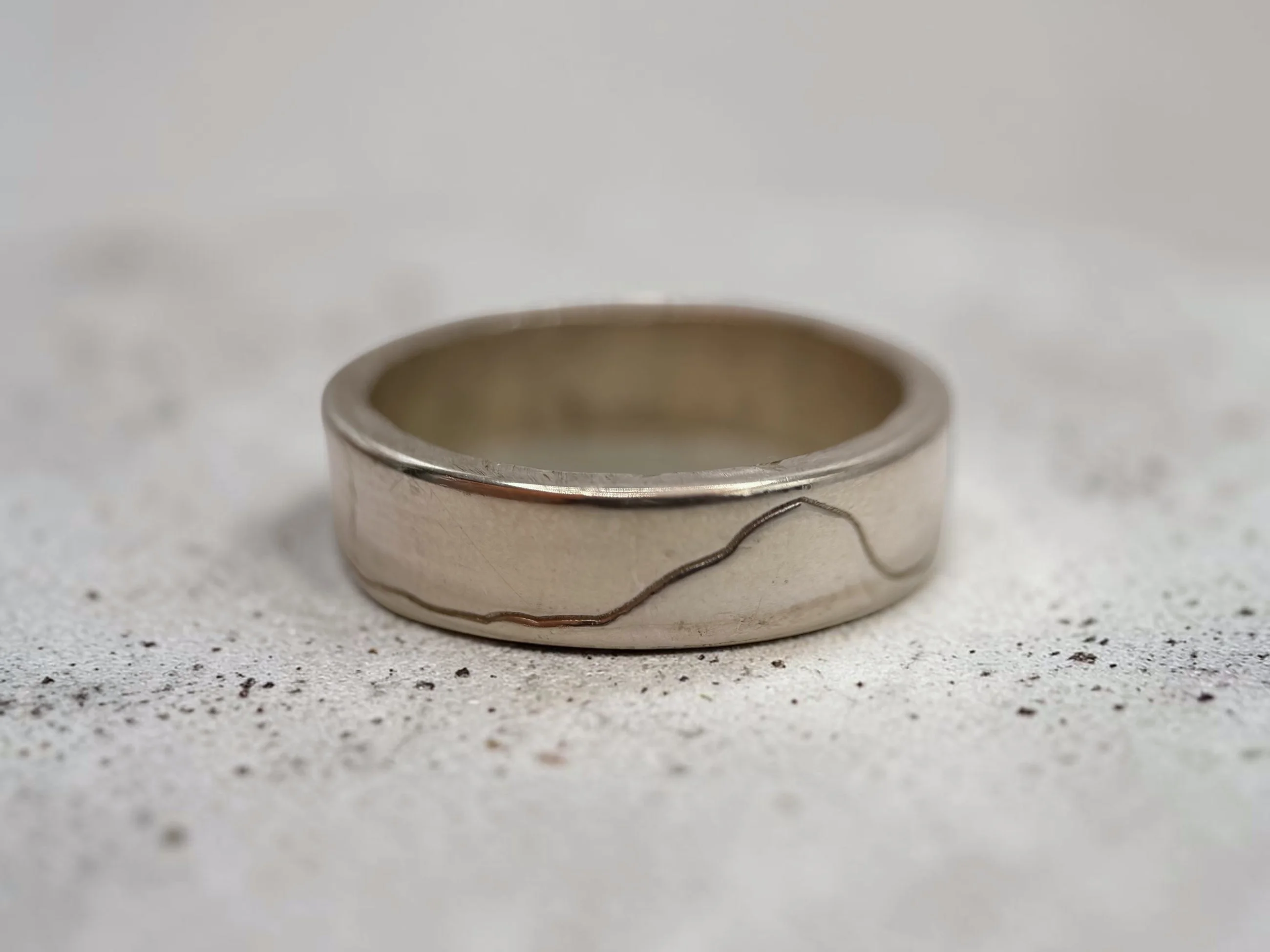 Yorkshire Three Peaks ring on a pale speckled surface, the fine engraved line running low across the band.