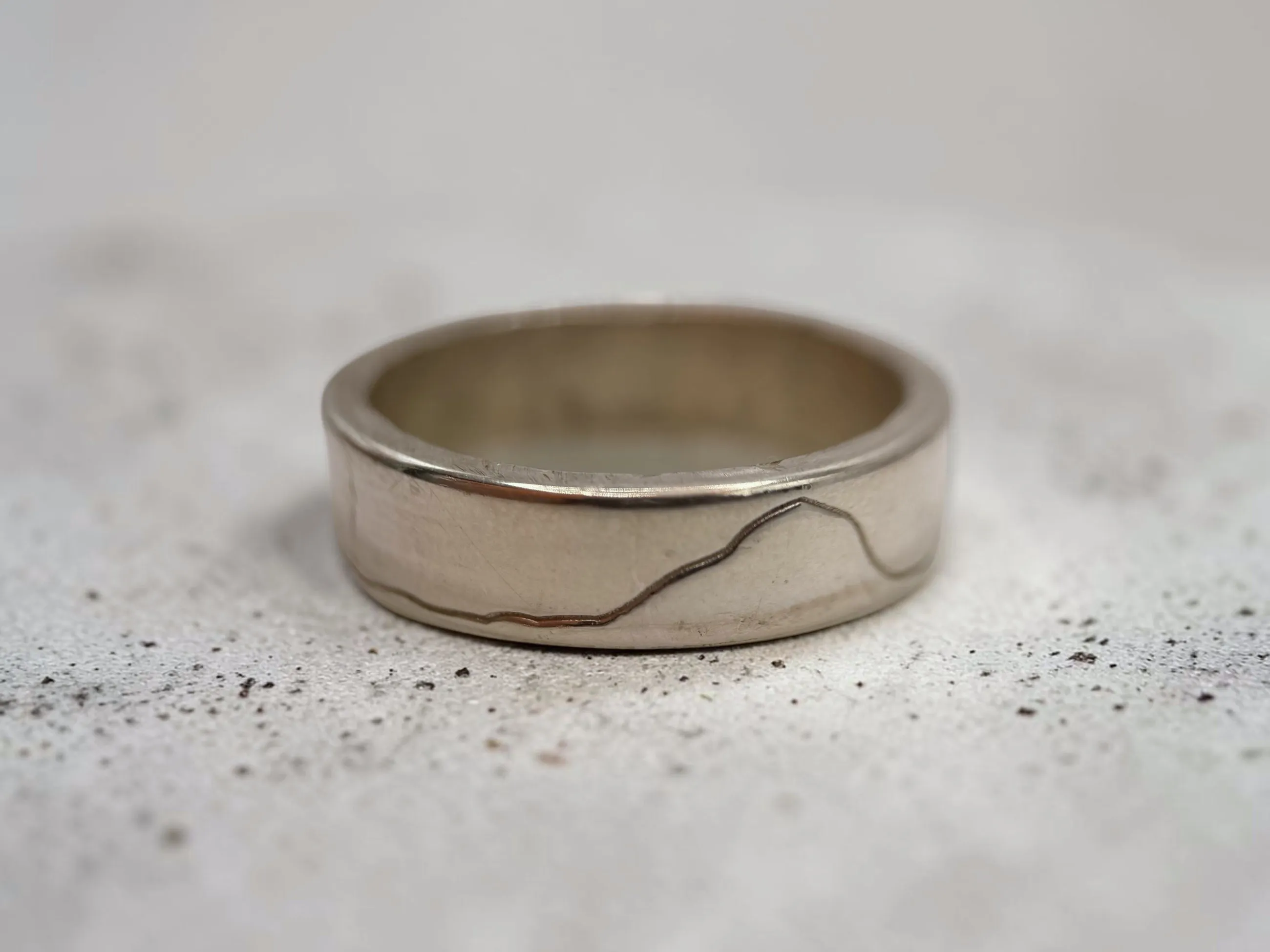 Yorkshire Three Peaks silver ring on a pale speckled surface, showing the engraved ridgeline.